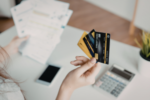 Person holding multiple credit cards while reviewing financial documents on a laptop, illustrating credit score management and personal finance decisions.